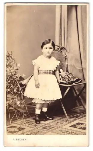 Fotografie E. Bieber, Hamburg, Gr. Bäckerstr. 26, Portrait kleines Mädchen im weissen Kleid mit Puppe auf dem Stuhl