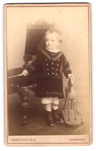 Fotografie Georg Wolf & Co., Hamburg, Alstertwiete 8, Portrait kleines Kind im Samtkleid mit Holzpferd und Gerte
