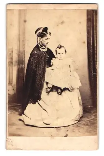Fotografie unbekannter Fotograf und Ort, Portrait Mutter im weiten Kleid mit kleiner Tochter auf dem Schoss, Mutterglück