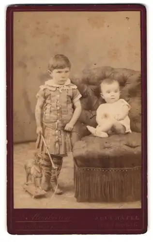 Fotografie A. Monbaron, Neuchâtel, 17, Rue de l`Hôpital, Portrait Mädchen im Kleid mit Kleinkind und Spielzeugpferd