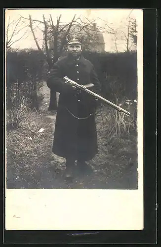 Foto-AK Soldat im Uniformmantel mit Schirmmütze und mit Gewehr, Uniformfoto