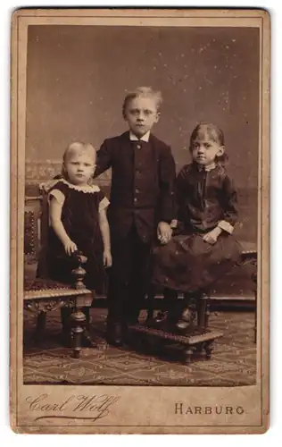 Fotografie Carl Wolf, Harburg, Portrait kleiner Junge und zwei Mädchen in zeitgenössischer Kleidung