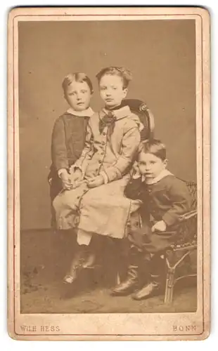 Fotografie W. Hess, Bonn, Coblenzer-Strasse 25, Drei Geschwister in festlicher Kleidung auf Stühlen