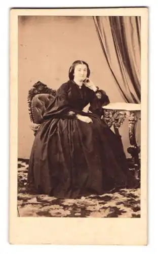 Fotografie unbekannter Fotograf und Ort, Portrait Dame im schwarzen Biedermeierkleid sitzend am Tisch