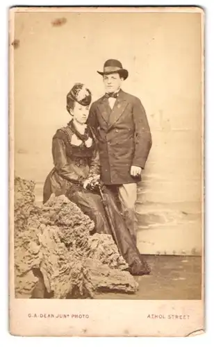 Fotografie G. A. Dean Jun., Douglas, britisches Paar in Biedermeierkleid vor einer Studiokulisse der Isle of Man