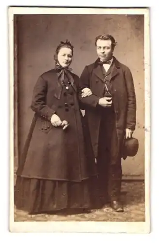 Fotografie unbekannter Fotograf und Ort, Portrait Paar in zeitgenössishcer Kleidung mit Mantel und Melone