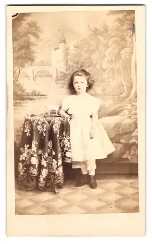 Fotografie Carl Schenk, Jena, Portrait kleines Mädchen im weissen Kleid posiert vor einer Studiokulisse