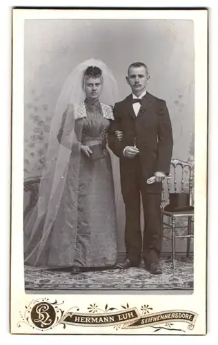 Fotografie Hermann Luh, Seifhennersdorf i. S., Portrait junge Eheleute im Hochzeitskleid mit Schleier und Anzug