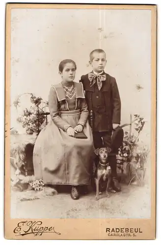 Fotografie E. Kupper, Radebeul, zwei Kinder in Biedermeierkleid mit jungem Hund im Atelier