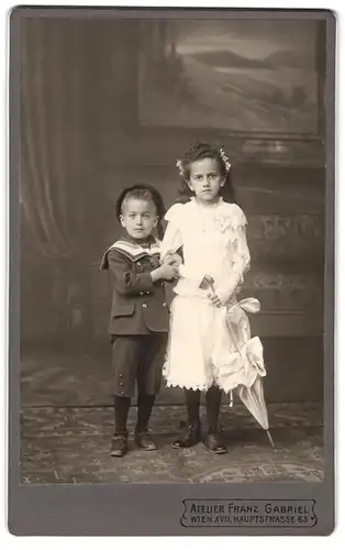 Fotografie FranzGabriel, Wien, Hauptstrasse 63, Knabe in Marineuniform nebst Mädchen im weissen Kleid mit Schirm