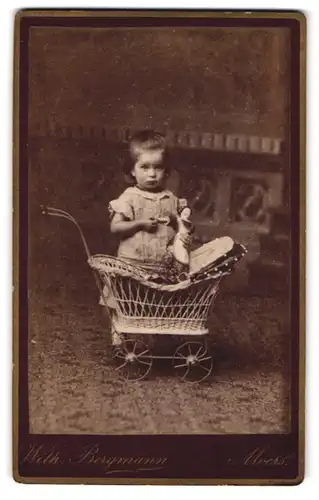 Fotografie Wilh. Bergmann, Moers, Portrait niedliches Mädchen im Kleid mit Puppe und Puppenwagen
