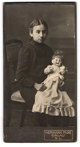 Fotografie Hermann Plog, Calau, Portrait Mädchen im schwarzen Kleid mit grosser Puppe auf dem Schoss