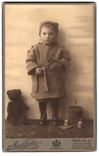 Fotografie Max Fischer, Berlin, Portrait kleines Mädchen im Wollkleid mit Teddybär und Buddel Spielzeug