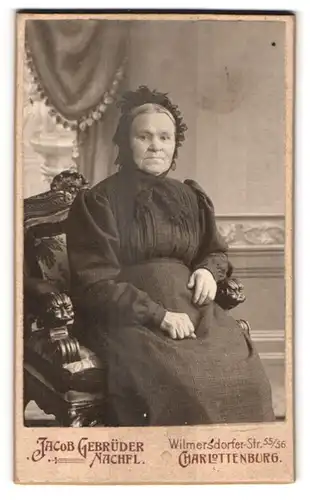 Fotografie Jacob Gebr. Nachf., Berlin, Portrait ältere Dame im schlichten Kleid mit Haube auf einem Löwenkopfstuhl