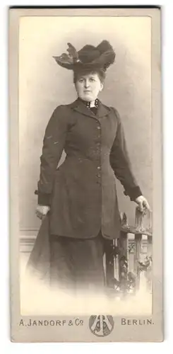 Fotografie A. Jandorf & Co., Berlin, Portrait Dame im dunklen Kleid mit Federhut posiert im Atelier
