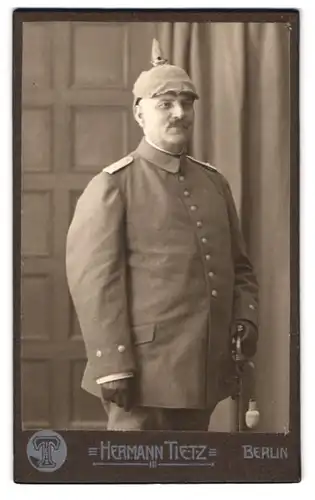 Fotografie Hermann Tietz, Berlin, Portrait Oberleutnant in Uniform mit Pickelhaube Tarnbezug