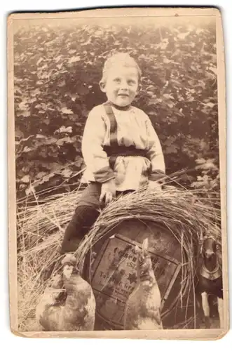 Fotografie Knabe auf Fass sitzend, Spielzeug-Pferd & Hühner