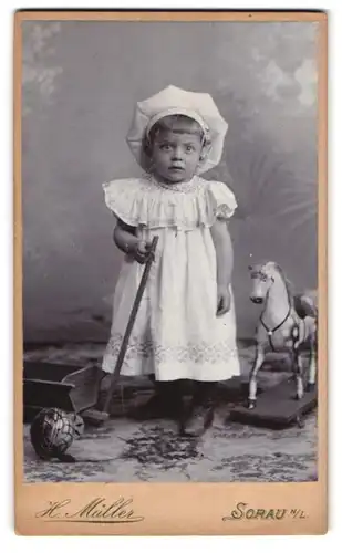 Fotografie H. Müller, Sorau N. L., Mädchen mit Haube nebst Spielzeugpferd & Bollerwagen