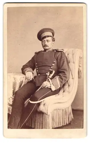 Fotografie Louis Füllgraf, Züllichau, Ulan in Uniform mit Epauletten & Säbel im Sessel sitzend