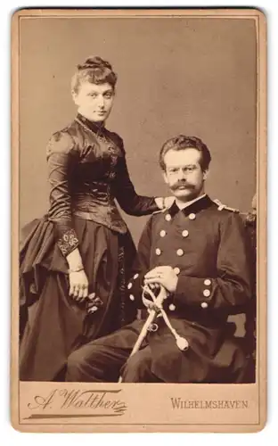 Fotografie Atelier Walther, Wilhelmshaven, Roonstr. 75, Offizier der kaiserlichen Marine mit Zwicker & Säbel nebst Frau