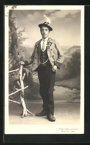 Foto-AK Mann in Tracht vor Gebirgslandschaft, Studiokulisse