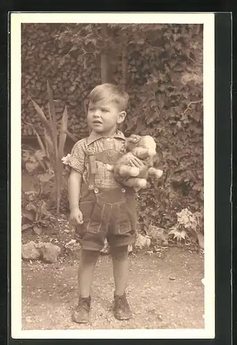 Foto-AK Kleiner Junge mit Latzhosen und Spielzeug im Arm