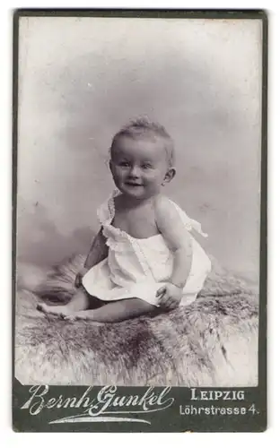 Fotografie Bernh. Gunkel, Leipzig, Löhrstr. 4, Portrait niedliches lachendes Baby auf einem Fell