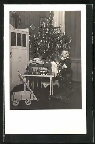 AK Bube sitzt vor dem Weihanchtsbaum auf einem Schaukelpferd