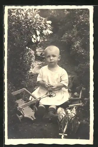 AK niedliches Mädchen mit Spielzeugpferdekutsche im Garten sitzend