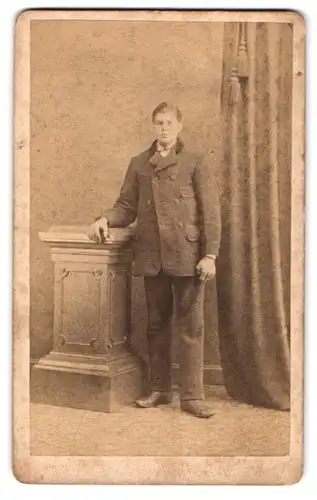 Fotografie G. Techel, Elmshorn, Portrait junger Herr im Wintermantel stehend an einer Säule