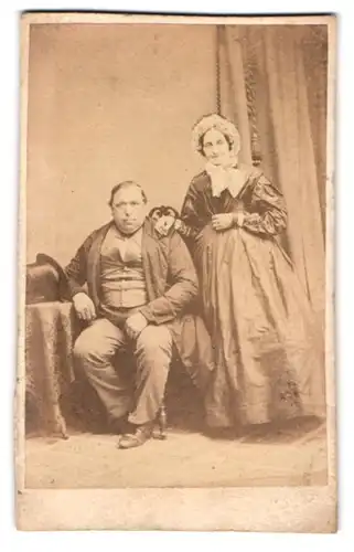 Fotografie J. Giese, Itzehoe, Portrait älteres Paar im Biedermeierkleid und Anzug mit Zylinder