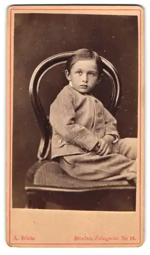Fotografie A. Schön, Breslau, Portrait junger Knabe im grauen Anzug sitzend auf einem Stuhl