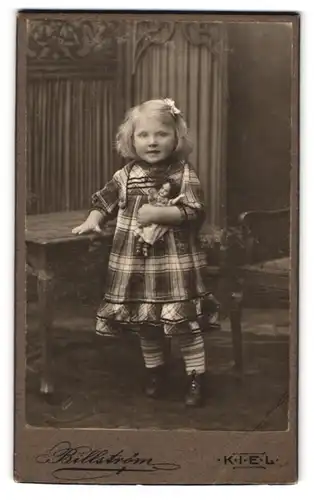 Fotografie Billström, Kiel, Holstenstr. 43, Portrait niedliches Mädchen im karierten Kleid mit ihre Puppe im Atelier