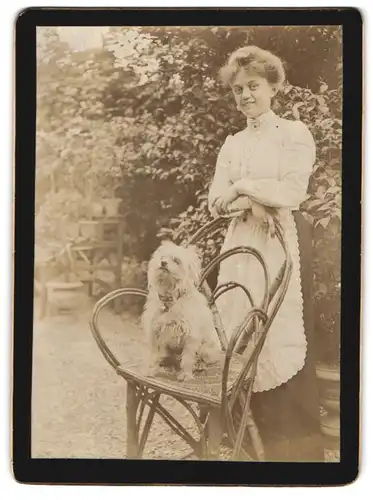 Fotografie unbekannter Fotograf und Ort, Portrait junge Frau im Hausmädchenkleid mit Hund auf dem Stuhl