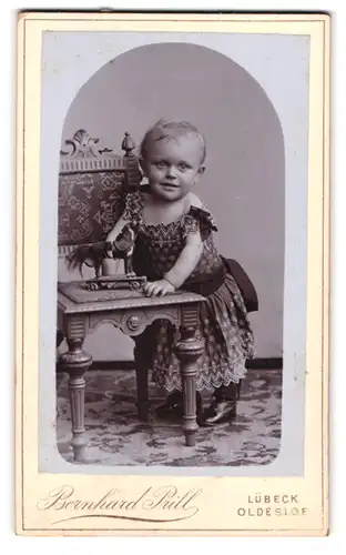 Fotografie Bernhard Prill, Lübeck, Breitestr. 97, niedliches Kleinkind mit Spielzeug Pferd auf dem Stuhl