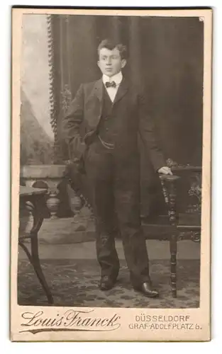 Fotografie Louis Franck, Düsseldorf, Graf-Adolf-Platz 6, Portrait eleganter junger Herr im Mantel mit Fliege