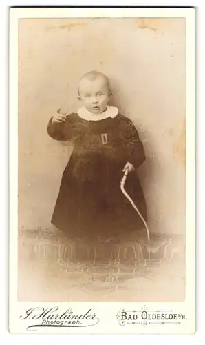 Fotografie J. Harländer, Bad Oldesloe i. H., Portrait niedliches Kleinkind im Kleid mit Spielzeug