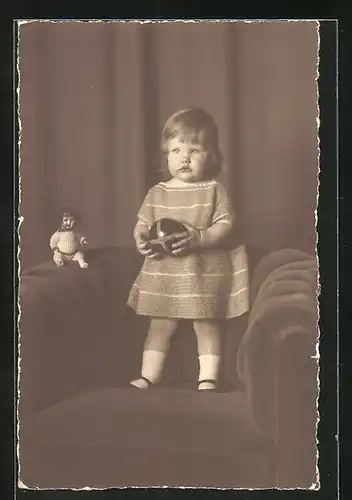 AK Puppe, kleines Mädchen mit ihrer Puppe auf einem Sessel