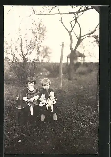 AK Puppe, zwei Mädchen im Garten auf einer Bank mit ihren Puppen