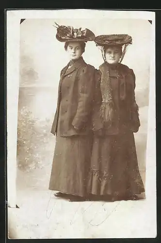 Foto-AK Studiokulisse, zwei Frauen in dunklen Mänteln und mit grossen Hüten