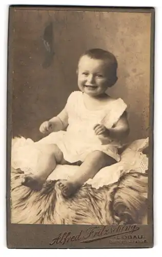 Fotografie Alfred Fritzsching, Löbau, Gartenstrasse, Portrait entzückendes lachendes Baby auf einem Kissen