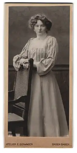 Fotografie Atelier E. Schwager, Baden-Baden, Portrait Dame im Edlen Kleid vor einem Stuhl
