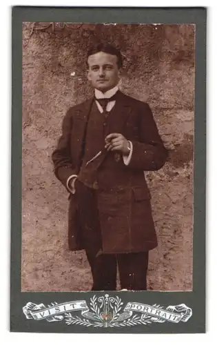 Fotografie Emil Drechsler, Marienberg i. Sa., Aussenaufnahme eleganter Herr mit Zigarre vor einer Wand