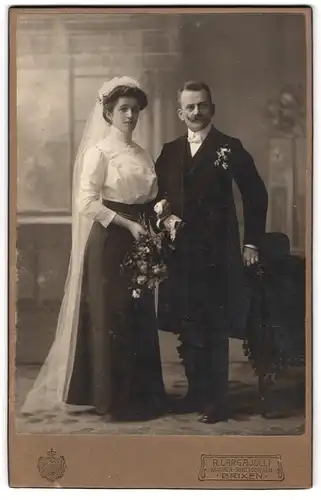 Fotografie R. Largajolli, Brixen, Adlerbrückenstr. 5, Portrait junges Paar in Hochzeitskleidung mit und Blumenstrauss