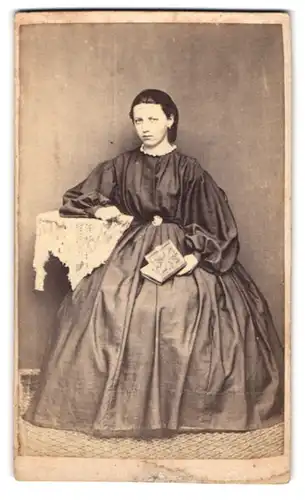 Fotografie unbekannter Fotograf und Ort, Portrait junge Frau im seidenen Biedermeierkleid mit Fotoalbum in der Hand