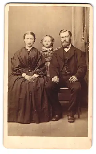 Fotografie unbekannter Fotograf und Ort, Portrait Mutter und Vater mit ihrer Tochter im karierten Kleid im Atelier