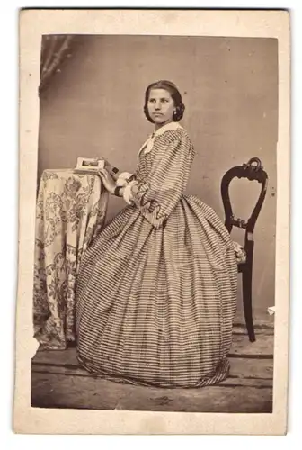 Fotografie unbekannter Fotograf und Ort, Portrait junge Frau im gestreiften Kleid sitzend am Tisch, Seitenprofil