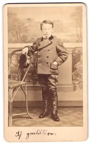 Fotografie E. Schroeter, Meissen, Obergasse 597, Portrait junger Knabe im Anzug mit Lederstiefeln mit Schirmmütze