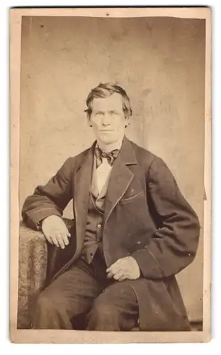 Fotografie unbekannter Fotograf und Ort, Portrait junger Mann im Anzug mit Fliege posiert sitzend im Atelier