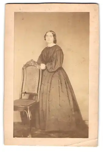 Fotografie unbekannter Fotograf und Ort, Portrait junge Dame im dunklen pünktchen Kleid stehend am Stuhl